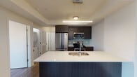Located at 1333 N Wells St in Chicago's vibrant Old Town neighborhood, this single-floor unit offers a thoughtfully designed contemporary interior. The open-concept living and kitchen area serves as the heart of the space, anchored by a large peninsula with a crisp white countertop and undermount sink, providing both additional workspace and a natural gathering point. The kitchen is outfitted with dark espresso cabinetry, stainless steel appliances including a French door refrigerator, gas range, and built-in microwave, complemented by a light blue subway tile backsplash that adds a subtle pop of color. Pendant and linear lighting illuminate the kitchen area, enhancing its modern aesthetic. Dark hardwood-style flooring runs throughout the living spaces, creating a cohesive, warm foundation. The bedroom features a generous closet and a large window offering city views. The bathroom is finished with large-format marble-patterned tile surrounding the tub-shower combination, dark tile flooring, a floating vanity with a white countertop, and a wide mirror. A dedicated in-unit laundry area with a stacked washer and dryer adds everyday convenience throughout this well-appointed space.