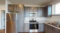 This single-floor unit showcases a cohesive, contemporary design throughout its well-appointed spaces. The kitchen is a functional centerpiece, equipped with stainless steel appliances including a refrigerator, electric range, and over-the-range microwave. Tall, wood-grain cabinetry in a warm gray-brown tone extends to the ceiling, maximizing storage, while marble-style countertops provide a clean, polished work surface. Wood-style plank flooring flows through the kitchen and living areas, adding warmth and continuity.

The living and dining area connects seamlessly to the kitchen, benefiting from natural light through multiple windows with horizontal blinds offering outdoor views of surrounding greenery. The bedrooms are carpeted for comfort and each features a ceiling fan and generously sized windows that invite natural light and outdoor views.

The bathrooms are well-designed, featuring the same wood-grain cabinetry and marble-style countertops found in the kitchen, with hardwood-style flooring, a full tub-shower combo, and large vanity mirrors. One bathroom includes access to a walk-in closet with built-in shelving and rod, adding practical storage. The overall ambiance is clean, neutral, and modern throughout.