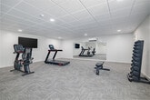 The fitness center at The Core Apartments in Nampa, Idaho, offers a well-appointed exercise space designed to meet a variety of workout needs. The room features a neutral, clean aesthetic with crisp white walls, a drop tile ceiling with recessed lighting, and durable patterned carpet throughout that adds a modern, functional feel underfoot.

The cardio section is equipped with a treadmill and a stationary upright bike, both positioned near a wall-mounted flat-screen television, making it easy to stay entertained during workouts. A dedicated split-system air conditioning unit ensures the space remains comfortable year-round. A full-width wall mirror spans one side of the room, visually expanding the space and allowing users to monitor their form during exercise.

The free weights area includes a complete dumbbell rack with a range of weights and an adjustable workout bench, providing ample options for strength training. A large sliding window along one wall allows natural light to filter into the space, enhancing the overall ambiance.

The room is generously sized, offering open floor space that allows for flexibility in exercise routines beyond the available equipment. Overall, this fitness center provides residents with a clean, functional, and well-equipped environment for maintaining an active lifestyle.