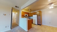This single-floor residence offers a practical and comfortable layout designed for everyday living. The open-concept living area is finished with neutral-toned wall-to-wall carpeting, creating a warm and cohesive atmosphere throughout. A ceiling fan overhead adds both functionality and a subtle design detail to the main living space.

The kitchen is a standout feature, equipped with warm-toned wood cabinetry offering ample storage, light-colored countertops, and a full suite of white appliances including a refrigerator, electric range, over-the-range microwave, and sink. The tile flooring in the kitchen provides a clean contrast to the carpeted living areas. A peninsula-style half-wall separates the kitchen from the living space, creating an open yet defined boundary between the two areas.

The living room benefits from generous natural light, courtesy of a sliding glass door with vertical blinds and an additional window fitted with horizontal blinds, offering views to the outdoors.

The bedrooms continue the carpeted flooring and neutral palette, each featuring a ceiling fan with a light fixture and windows that invite natural light. Closet access is conveniently located within each bedroom.

The bathroom is finished with tile flooring and includes a vanity with white cabinetry and a countertop, toilet, and grab bars, reflecting a practical and accessible design. The overall ambiance of the space is clean, neutral, and move-in ready.
