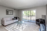 This single-floor residence offers a practical and comfortable layout across several well-defined spaces. The living room serves as the central gathering area, finished with wall-to-wall carpet, a textured ceiling, and neutral gray walls. A standout feature is the full-width sliding glass door that opens to a private balcony overlooking mature trees, filling the room with natural light and outdoor views. A dedicated dining area with a ceiling fan adjoins the living space, providing a functional transition toward the kitchen.

The galley-style kitchen is efficiently designed with dark wood cabinetry lining both sides, light countertops, tile flooring, and standard appliances including an electric range and dishwasher. Two bedrooms are carpeted and share a similar neutral palette, each with windows that bring in natural light. Both offer adequate space for furnishings and storage.

Two bathrooms serve the unit; one features a tub-shower combination with mosaic tile flooring, while the second is a compact stand-up shower bathroom, also with mosaic tile flooring. Consistent textured ceilings and neutral wall tones unify the space throughout, creating a cohesive and functional living environment.