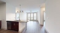 This well-appointed 910-square-foot, single-story apartment offers 1 bedroom, 2 bathrooms, and a thoughtfully designed open-concept layout. The combined kitchen and living area serves as the heart of the unit, featuring rich dark-wood cabinetry, a granite-topped island with a built-in sink, stainless steel appliances including a French door refrigerator and microwave, subway tile backsplash, and pendant lighting — all set over durable hardwood-style flooring that extends throughout the unit. The primary bedroom measures 140 square feet and is bathed in natural light through large windows with outdoor views, complemented by a ceiling fan. It connects to a full en-suite bathroom boasting granite countertops, dark wood vanity cabinetry, a glass-enclosed shower, and direct access to a walk-in closet with wire shelving. A second full bathroom includes a tiled tub-shower combination, matching dark wood cabinetry, and granite countertops. The dedicated laundry room houses a full-size washer and dryer with overhead shelving. Two closets provide ample storage throughout. Neutral walls and consistent flooring create a cohesive, modern ambiance across the entire unit.