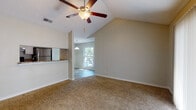 This single-story residence offers a thoughtfully arranged floor plan that balances open communal areas with private living spaces. The living room serves as the centerpiece of the home, distinguished by soaring vaulted ceilings and a ceiling fan that enhances the sense of airiness. Soft, neutral-toned carpet covers the floor, and a large sliding glass door fitted with vertical blinds allows abundant natural light to fill the room while providing outdoor access.

The kitchen is efficiently designed with white cabinetry, granite-style countertops, and stainless steel appliances including a refrigerator and electric range. A pass-through counter connects the kitchen to the living area, promoting an open, communicative flow between the two spaces. An adjacent dining area benefits from a pendant light fixture and a window overlooking greenery outside.

The bedrooms are carpeted and feature neutral walls, natural light from windows with blinds, and textured ceilings. Each room offers a clean, versatile canvas suitable for various furnishing arrangements.

The bathroom includes a full-size tub and shower combination with white square tile surround, wood-look vinyl flooring, and chrome hardware accents. Throughout the home, warm neutral tones and practical finishes create a cohesive, move-in-ready environment.