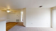 This single-floor unit offers a functional and comfortable layout designed for everyday living. The open living area is carpeted and features a ceiling fan, sliding glass door that fills the space with natural light, and a seamless transition to wood-style flooring near the entryway. A breakfast bar peninsula connects the living area to the galley-style kitchen, which is fitted with white cabinetry, a double-basin sink, electric range, refrigerator, dishwasher, and durable wood-look flooring beneath overhead fluorescent lighting. An electrical panel is conveniently located within the kitchen corridor, which also leads to an exterior door. The bedrooms are carpeted and bright, each featuring windows with vertical blinds that allow for adjustable natural light and outdoor views of surrounding greenery. The bathroom is appointed with a vanity featuring a wide mirror, under-sink cabinetry, a toilet, and a full bathtub with shower combination, all set on warm wood-style flooring. A textured ceiling and neutral wall tones throughout the unit contribute to a clean, versatile aesthetic. Built-in closets and HVAC vents are present throughout, adding to the overall practicality of the space.