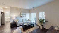 This single-floor residence offers a well-designed layout across multiple rooms, blending modern finishes with a comfortable, neutral aesthetic throughout. The living room serves as a central gathering space, featuring dark hardwood-style flooring, vaulted ceilings, and sliding glass doors that open to a private balcony with outdoor views, allowing natural light to fill the room. A wall-mounted television and dedicated media storage complete the space.

The kitchen is thoughtfully appointed with white shaker cabinetry, a white subway tile backsplash, dark countertops, and stainless steel appliances including a refrigerator, range, and microwave. A peninsula with seating for three provides casual dining space, complemented by pendant and track lighting overhead.

The primary bedroom features soft carpeting, neutral wall tones, and direct access to a walk-in closet area and an en-suite bathroom equipped with a tub-shower combination, wood-style flooring, a tall linen storage cabinet, and a single-sink vanity with a large mirror. Additional bedrooms offer carpeted flooring, natural light from windows, and ample space. A second bathroom provides a dual-sink vanity with white cabinetry, a large mirror, and wood-style flooring, presenting a clean and functional design throughout.