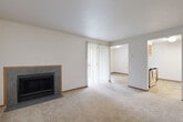 Located at 900 SE Park Crest Ave in Vancouver, Washington, this 2-bedroom, 1-bathroom residence offers a practical and comfortable single-floor layout. The main living room is a welcoming space anchored by a slate-tile-surround fireplace with a wood-trimmed mantle and plush wall-to-wall carpeting underfoot. A sliding glass door with vertical blinds fills the room with natural light and provides outdoor access. The layout flows seamlessly into a secondary living area, offering flexible use of space. The kitchen features warm honey-toned wood cabinetry, white countertops, a double-basin sink, and durable tile flooring, with full appliances including a dishwasher and refrigerator. The full bathroom includes a tub-shower combination with a curtain enclosure. Both bedrooms are carpeted and feature neutral walls, baseboard heating, and ample natural light from windows with vertical blinds. The primary bedroom includes a built-in closet with sliding wood-panel doors and a clothing rod. A dedicated closet area and an additional tiled room with a window provide extra storage and utility options. Baseboard heating is present throughout, ensuring year-round comfort in this clean, well-organized residence.