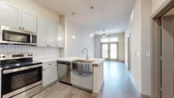 This 1-bedroom, 1-bathroom residence in Georgetown, TX offers a thoughtfully designed open-concept floor plan with modern finishes throughout. The kitchen is a standout feature, showcasing shaker-style cabinetry in a soft gray-white tone, a herringbone tile backsplash, white quartz countertops, and a suite of stainless steel appliances including a French door refrigerator, electric range, microwave, and dishwasher. A peninsula with a stainless steel farmhouse sink and pendant lighting above serves as both a functional workspace and a natural divider between the kitchen and living area. Light wood-look flooring flows seamlessly throughout the entire unit, enhancing the bright, cohesive aesthetic. The living area benefits from natural light streaming through double glass entry doors and is equipped with a ceiling fan. The bedroom is a calm, well-lit retreat with a large window fitted with blinds. It connects directly to a full bathroom featuring a dual-sink vanity with quartz countertops, black hardware accents, a soaking tub with tiled surround, and a dedicated walk-in closet with built-in shelving. The clean, neutral color palette and contemporary finishes give the entire space a fresh, move-in-ready feel.