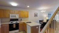 This two-story residence offers a well-designed layout that balances practicality and comfort across both levels. The main living area showcases an open-concept kitchen and dining space that seamlessly connect to create an inviting, functional environment. The kitchen is outfitted with warm honey-toned wood cabinetry providing ample storage, a full suite of appliances including an electric range, built-in microwave, dishwasher, and a double-basin sink set into a peninsula that doubles as a prep and serving area. Light countertops complement the cabinetry and contribute to the kitchen's bright, clean aesthetic. Recessed and flush-mount ceiling lighting ensures the space is well-illuminated throughout. Adjacent to the kitchen, the dining area is anchored by an elegant chandelier that adds a refined touch to the space. A framed landscape artwork adorns the wall, contributing to the warm and welcoming ambiance. The staircase, visible from the main level, connects to the second floor, hinting at additional living spaces above. Overall, the residence presents a cohesive and functional interior suited for everyday living.
