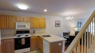 This two-story residence offers a well-designed layout that balances practicality and comfort across both levels. The main living area showcases an open-concept kitchen and dining space that seamlessly connect to create an inviting, functional environment. The kitchen is outfitted with warm honey-toned wood cabinetry providing ample storage, a full suite of appliances including an electric range, built-in microwave, dishwasher, and a double-basin sink set into a peninsula that doubles as a prep and serving area. Light countertops complement the cabinetry and contribute to the kitchen's bright, clean aesthetic. Recessed and flush-mount ceiling lighting ensures the space is well-illuminated throughout. Adjacent to the kitchen, the dining area is anchored by an elegant chandelier that adds a refined touch to the space. A framed landscape artwork adorns the wall, contributing to the warm and welcoming ambiance. The staircase, visible from the main level, connects to the second floor, hinting at additional living spaces above. Overall, the residence presents a cohesive and functional interior suited for everyday living.