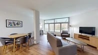 Located at 100 Reserve Rd in Danbury, CT, this thoughtfully designed one-bedroom, one-bathroom residence offers a clean, modern aesthetic throughout. Warm hardwood flooring flows continuously across the entire floor plan, creating a cohesive and inviting atmosphere.

The open-concept living and dining area is a standout, anchored by expansive floor-to-ceiling windows with transom glass panels that flood the space with natural light and frame serene views of the surrounding landscape. The living area comfortably accommodates seating and entertainment arrangements, while a dedicated dining space adds everyday functionality.

The kitchen is well-appointed with dark espresso cabinetry, white subway tile backsplash, stainless steel appliances including a refrigerator, range, microwave, and dishwasher, and ample counter space — ideal for both everyday cooking and entertaining.

The bedroom features the same generous window configuration as the living area, offering abundant natural light and outdoor views. A wall-mounted climate control unit ensures year-round comfort. The clean, neutral palette creates a calm and restful environment.

The bathroom is finished with a full tub-shower combination and clean white fixtures. An entrance area provides a practical transition into the home. Overall, the residence presents a bright, modern living experience with quality finishes throughout.