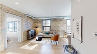Located at 1554 Midway Pkwy in Saint Paul, MN, this one-bedroom, one-bathroom unit masterfully blends industrial character with modern finishes. The living room immediately impresses with its sweeping exposed brick walls, polished concrete-look light wood flooring, and eye-catching exposed silver ductwork running along the ceiling — hallmarks of loft-inspired design. Large black-framed windows flood the space with natural light and offer views of the surrounding neighborhood. The open kitchen is efficiently laid out with crisp white upper cabinetry, two-tone lower cabinets, stainless steel appliances including a full-size refrigerator and dishwasher, and a clean white countertop with an undermount sink. The bedroom is a calm, well-lit retreat featuring soft carpet, a sliding closet door, and a large window that invites in ample daylight. Exposed ductwork continues here, maintaining the unit's cohesive industrial aesthetic. The bathroom is thoughtfully appointed with warm wood-tone flooring, a modern gray vanity, a wall-mounted mirror with vanity lighting, and a shower/tub combination. Throughout the unit, the contrast of raw brick and polished modern finishes creates a distinctive urban ambiance that is both functional and full of character.