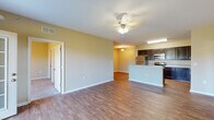 This single-floor unit features an open-concept layout that connects the living area and kitchen, creating a cohesive and functional living space. The living area is finished with wood-style flooring and neutral-toned walls, and is equipped with a ceiling fan with light fixture. French doors provide access to a private balcony, allowing natural light to fill the room. The kitchen is well-appointed with dark espresso-toned cabinetry offering generous upper and lower storage, stainless steel appliances including a refrigerator, electric range, and microwave, as well as light-toned countertops. A peninsula counter separates the kitchen from the living space, adding additional workspace and a visual boundary between the two areas. The bathroom includes a full soaking tub with a surround enclosure, dark wood vanity cabinetry, and wood-style flooring. A dedicated laundry room with hookups and wire shelving provides added convenience. The unit also includes a spacious walk-in closet with wire shelving systems extending along multiple walls, and carpeted flooring for comfort underfoot.