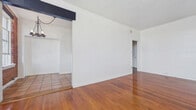 Located at 1843 North Cherokee Avenue in the heart of Hollywood, Los Angeles, this 570-square-foot single-floor unit blends classic character with functional design. The living room is a standout space, showcasing rich, polished hardwood floors that reflect natural light streaming through large multi-pane sash windows set within a striking exposed red brick accent wall — a defining architectural feature that adds warmth and urban charm to the unit. A built-in closet alcove provides practical storage within the living area. The kitchen features warm terracotta tile flooring, white cabinetry, a stainless steel refrigerator, and a peninsula with open shelving underneath, offering both storage and a casual workspace. Two hallways connect the rooms, ensuring a logical and efficient flow throughout the unit. The bathroom is finished with classic white subway wall tiles, a full soaking bathtub with overhead shower, a modern toilet, and a distinctive black-and-white hexagonal mosaic tile floor that adds a timeless, vintage aesthetic. The overall ambiance of the unit is one of classic Hollywood character, combining original architectural details with clean white walls and practical finishes throughout.