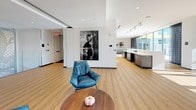 Located at 500 Rutherford Ave in Boston's Charlestown neighborhood, this single-floor lounge space showcases a thoughtfully designed interior that seamlessly blends contemporary aesthetics with functional comfort. The space is characterized by warm hardwood-style flooring, crisp white ceilings with recessed lighting, and an open layout that encourages both relaxed socializing and quiet retreat.

One of the most striking features is the expansive wall of floor-to-ceiling glass doors that floods the interior with natural light and opens directly onto an outdoor terrace, offering views of the surrounding Boston skyline and neighborhood. A warm wood ceiling detail frames this glazed facade, enhancing the connection between indoors and out.

The lounge area is furnished with an eclectic mix of seating, including leather accent chairs, plush high-back armchairs in rich burgundy and grey tones, and a generous sectional sofa, all arranged atop a boldly patterned area rug. A built-in media wall with a flat-screen television anchors one end of the space. Curated large-format artwork adds a gallery-like quality to the interior. An adjacent kitchenette and a decorative glass-paneled staircase railing further contribute to the space's polished, contemporary character.
