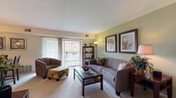 This single-floor residence offers a thoughtfully designed layout that balances comfort and functionality. The living room is a welcoming space adorned with sage-green accent walls, soft carpeting, and a sliding glass door that opens to a private balcony, allowing natural light to flow in and offering views of the surrounding exterior. A dedicated dining area sits adjacent to the living room, complete with a stylish pendant chandelier and its own sliding door, further enhancing the sense of openness.

The kitchen features rich, dark wood cabinetry set against light countertops, providing ample storage and workspace. White appliances, including a gas range and dishwasher, complement the tile flooring and keep the space clean and practical.

Both bedrooms are generously sized with plush carpeting and ceiling fans. The primary bedroom features a tray ceiling detail and wide windows that bring in views of lush greenery, while the second bedroom includes a walk-in closet for added convenience. Each room provides a calm, restful atmosphere.

The bathroom is finished with classic white tile surrounding the tub-shower combination, mosaic tile flooring, and a clean, bright aesthetic. Throughout the residence, neutral tones and consistent carpeting create a cohesive and inviting ambiance.