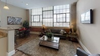 Located at 34 Franklin in Nashua, NH, this single-floor residence blends industrial character with modern comfort. The living area is a standout, featuring floor-to-ceiling multi-pane windows that flood the space with natural light and offer open views of the surrounding cityscape. Exposed brick accents and hardwood-style flooring reinforce the loft-inspired aesthetic throughout the main living and dining areas.

The kitchen is thoughtfully designed with white shaker cabinetry, granite countertops, stainless steel appliances including a French door refrigerator and built-in microwave, and a breakfast bar with seating — ideal for casual dining. Adjacent to the kitchen, the dining area accommodates a full-sized table and benefits from the same warm, open ambiance as the living space.

The bedrooms are finished with plush carpet, neutral tones, and ample closet space, including a walk-in closet in the primary bedroom, providing a quiet retreat from the main living areas. The bathroom features granite countertops, a white vanity, and the added convenience of an in-unit stacked washer and dryer. Clean lines, warm neutral walls, and consistent high-quality finishes tie the entire residence together into a cohesive and comfortable living environment.