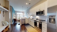 This single-floor residence showcases a thoughtfully designed open-concept layout that seamlessly connects the kitchen, dining, and living areas. The kitchen is a standout feature, outfitted with white shaker cabinetry, granite countertops, a herringbone-patterned tile backsplash, and a full suite of stainless steel appliances, including a French door refrigerator, range, built-in microwave, and dishwasher. Pendant lighting above the peninsula adds a refined touch while providing additional seating and prep space. Rich hardwood flooring flows throughout the main living areas, grounding the space with warmth.

The living area is distinguished by a striking teal accent wall adorned with geometric wall art, creating a bold, curated atmosphere. Large windows invite abundant natural light and outdoor views, enhancing the open, airy feel of the space.

The bedroom features a deep terracotta-red accent wall that adds dramatic warmth, complemented by a ceiling fan and sheer window treatments that allow soft, diffused light. The en-suite bathroom is finished with hexagonal floor tile, white vanity cabinetry with granite counters, a large mirror, and a walk-in glass shower with white subway tile surround, offering a clean, modern aesthetic.