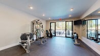 Located at 14735 Stable Gate Pl in Louisville, KY, this dedicated fitness center offers a well-appointed single-room workout space designed to support a comprehensive exercise routine. The room features durable rubber flooring throughout, providing a safe and functional surface ideal for a wide range of physical activities.

The space is outfitted with a robust selection of equipment, including a Hoist multi-station cable machine for strength training, a Spirit treadmill, a recumbent exercise bike, a rowing machine, and additional resistance training attachments. An exercise reference chart is mounted on the wall for guided workout routines, and a wall-mounted television provides entertainment during sessions.

A full-width wall mirror spans one side of the room, visually expanding the space and allowing users to monitor their form during exercise. Recessed ceiling lighting ensures the area is well-lit throughout. Large glass sliding doors open to an outdoor balcony furnished with seating, offering natural light and scenic views of surrounding greenery — a refreshing complement to the indoor workout environment.

Access to the fitness center is facilitated through a set of double glass-panel doors connected to a stairwell, making it conveniently reachable. The clean, neutral-toned walls and thoughtful layout create an organized and motivating atmosphere well-suited for daily fitness use.