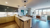This single-floor residence showcases a thoughtfully designed open-concept layout that seamlessly connects the kitchen, dining, and living areas. The kitchen is a standout feature, equipped with stainless steel appliances, a gas range, a large center island with a white quartz countertop, and a striking marble-effect backsplash. Upper cabinetry in dark charcoal contrasts elegantly with warm wood-toned lower cabinets, while pendant lighting adds a refined touch.

The living area flows naturally from the kitchen and dining space, offering access to a private balcony through floor-to-ceiling sliding glass doors that flood the room with natural light and provide views of the surrounding neighborhood. The dining area sits centrally between the kitchen and living room, creating an ideal space for entertaining.

Multiple bedrooms are present, each featuring hardwood-style flooring, generous window configurations with balcony access, and ample space. One bedroom includes a dedicated desk area, making it well-suited as a home office.

The hallway connects rooms with curated artwork, adding character to the transitional spaces. Bathrooms feature wood-toned tile surrounds, soaking tubs, separate glass-enclosed showers in the primary bath, light blue vanities with white countertops, and wood-style flooring throughout, creating a cohesive, spa-inspired aesthetic.