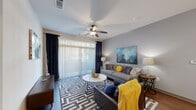 This single-floor residence offers a thoughtfully designed layout comprising two bedrooms, two bathrooms, a combined kitchen and living area, and two closets. The living room is a welcoming space anchored by dark hardwood flooring, a ceiling fan with integrated lighting, and a large sliding glass door fitted with vertical blinds and navy curtain panels that allow abundant natural light to fill the room.

The kitchen is well-equipped with dark espresso cabinetry, a subway tile backsplash, stainless steel appliances including a range, microwave, and refrigerator, and a granite-topped island with a double sink and pendant lighting above, providing both functionality and a clean aesthetic.

The primary bedroom offers a comfortable footprint with carpeted flooring, a ceiling fan, and a window with exterior views. The second bedroom mirrors the same carpeted finish and ceiling fan configuration. Both bathrooms feature granite countertops, dark wood vanities, large framed mirrors, and hardwood-style flooring. Each bedroom is paired with a dedicated closet, contributing to practical storage throughout the unit. The overall design reflects a modern, cohesive style with neutral tones and contemporary finishes.