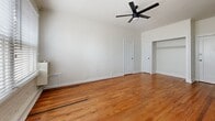 Located at 245 N Kenmore Ave in the Koreatown neighborhood of Los Angeles, this single-floor unit offers an efficient and well-appointed layout comprising a living room, kitchen, and two bathrooms. Warm hardwood flooring runs throughout the main living areas, lending a classic character to the space. The living room is bright and open, featuring white walls, a sleek ceiling fan, and windows with horizontal blinds that allow natural light to filter in. An exposed painted brick accent wall adds a touch of industrial charm. A built-in shelving unit near the entryway provides convenient storage alongside a dedicated closet space. The kitchen is outfitted with crisp white shaker-style cabinetry, a stainless steel undermount sink, and a stainless steel refrigerator, all complemented by a window that brings in additional natural light. Both bathrooms feature clean, white subway tile surrounds in the tub-shower combinations, classic black-and-white mosaic tile flooring, and chrome fixtures, delivering a timeless aesthetic. The overall ambiance is bright, clean, and functional, with consistent design elements tying the space together cohesively.