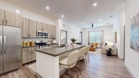 Located at 2031 Synergy Ln in Sarasota, FL, this well-appointed 2-bedroom, 2-bathroom residence offers a thoughtfully designed single-floor layout with modern finishes throughout. The open-concept kitchen and living area serves as the heart of the home, anchored by a large center island with quartz-style countertops and seating for multiple guests. The kitchen is outfitted with stainless steel appliances, light wood cabinetry with black hardware, a subway tile backsplash, and ample storage. Wood-look plank flooring flows seamlessly throughout the entire residence, lending warmth and visual continuity. The living room is bright and airy, benefiting from generous natural light through large windows dressed with linen drapes. A ceiling fan adds comfort to the open living space. Both bedrooms are generously proportioned, each featuring high ceilings and direct access to walk-in closets with built-in shelving and hanging systems. The primary bedroom connects to a dedicated bathroom, while the second bathroom offers a full tub-shower combination. Both bathrooms feature wood-toned vanities with quartz countertops and matching black hardware, maintaining a cohesive modern aesthetic. Two closets provide excellent storage capacity throughout the residence.