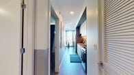 Located in Chicago's South Loop at 1216–1248 S Indiana Ave, this single-floor unit showcases a contemporary design with clean lines, light wood flooring, and a neutral palette throughout. A long entry corridor leads into the space, with the galley-style kitchen positioned along one wall. The kitchen is outfitted with light wood cabinetry extending to the ceiling, a gas range, integrated microwave, and light-toned countertops with under-cabinet lighting that adds a warm, functional glow.

The living area features an elevated loft-style opening above, framed by a curtain rod with a rust-colored drape, adding visual depth to the room. The living space accommodates comfortable seating and a wood media console, with large windows drawing in natural light and offering city views. The overall atmosphere is calm and modern, with curated wall art reinforcing a stylish aesthetic.

The bedroom is thoughtfully appointed with a structured headboard wall, dual bedside lighting, and framed artwork. A sliding door reveals a well-organized walk-in closet with built-in shelving. The bathroom features a spacious walk-in shower enclosed in light vertical tile, with a dark tiled floor and clean, minimalist fixtures completing the refined look.