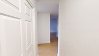 Located at 65-77 Prospect Street in Stamford, Connecticut, this two-bedroom residence offers a clean, modern aesthetic across a thoughtfully arranged single-level floor plan. Light hardwood flooring runs throughout the entire space, complementing the crisp white walls and trim to create a bright, cohesive atmosphere.

A central hallway connects the main living areas and bedrooms, providing a logical and efficient flow throughout the home. The generously sized primary bedroom is bathed in natural light from a large window fitted with horizontal blinds, and includes a dedicated closet, adding practical storage. The second bedroom also features a window with views of the surrounding Stamford streetscape, and benefits from its own wall unit and baseboard heating system.

The living area is open and well-proportioned, with natural light streaming in through windows that frame views of the neighboring cityscape. White walls and high ceilings contribute to an airy, uncluttered feel throughout. The kitchen, visible in the floor plan, features white cabinetry and a marble-style countertop, lending a refined touch to the space.

Clean lines, neutral finishes, and an abundance of natural light define the overall ambiance of this Stamford residence, offering a move-in-ready environment in a convenient downtown location.