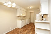 This single-floor space is thoughtfully laid out to maximize functionality across its living areas. The kitchen is equipped with white cabinetry, a double basin sink, a white electric range, a dishwasher, and an overhead microwave. Wood-look flooring anchors the kitchen and flows into the hallway, which connects the main living areas and features multiple doorways leading to adjacent rooms.

The bedrooms are carpeted in neutral tones and receive natural light through wide windows fitted with vertical blinds. One bedroom is outfitted with a ceiling fan and light fixture, while another features a louvered closet door visible from the hallway. Each room offers a comfortable sense of space suited for various furniture arrangements.

The bathroom includes a full-size soaking tub with an overhead shower, surrounded by classic white square tile that extends from floor to ceiling. The vanity area features a white under-mount sink set into a light countertop, white cabinetry with ample storage, wall-mounted sconce lighting, and a large mirror. Wood-look flooring continues throughout the bathroom, adding a warm contrast to the bright fixtures. Neutral wall tones and clean finishes are consistent throughout the space.
