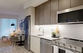 This one-bedroom, one-bathroom unit at Citizen On Jasper is thoughtfully designed to maximize every square foot of its compact footprint. The layout flows efficiently from the entry through the kitchen and into the living area, creating a cohesive and functional open-concept space.

The kitchen is a standout feature, outfitted with full-size stainless steel appliances including a French door refrigerator, gas range, built-in microwave, and dishwasher. Two-tone cabinetry pairs warm wood-grain upper cabinets with light lower units, complemented by a white subway tile backsplash, under-cabinet lighting, and a clean quartz countertop. Light wood-style luxury vinyl plank flooring runs throughout the entire unit, adding warmth and continuity.

The living area accommodates both lounging and dining, with a large window that filters in natural light and provides a bright, airy ambiance. White walls and minimalist finishes keep the space feeling open.

The private bedroom offers a comfortable retreat with a window, closet, and clean white walls. The overall design aesthetic throughout the unit is modern and contemporary, with an emphasis on efficient use of space and high-quality finishes.