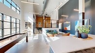 Located at 300 Commerce Ave in LaGrange, Georgia, this single-floor community amenity space delivers a striking blend of industrial and contemporary design across a generously sized open-plan layout. Soaring ceilings with exposed ductwork and structural columns set a dramatic tone, while an array of suspended linear pendant lights and ceiling fans provide both functional illumination and visual interest overhead.

The space is organized into several distinct yet open zones. A game area anchored by a rich wood-framed billiards table sits beneath a bold dark-painted accent wall adorned with colorful modern artwork. Adjacent to it, a comfortable lounge area features a sage green sofa, cognac leather accent chairs, and a woven area rug, creating an inviting spot for conversation and relaxation. A café-style seating zone near the entrance offers banquette and bistro seating alongside a warm natural wood feature wall with gold pendant sconces.

Polished concrete floors run throughout, contributing to the space's clean, contemporary feel. Floor-to-ceiling black-framed glass windows and doors flood the interior with abundant natural light and provide views of the outdoor amenity area beyond. A glass-partitioned interior section adds architectural depth, while a built-in cabinetry station and lush indoor greenery round out the refined, welcoming atmosphere of this well-appointed community gathering space.