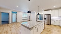 This single-story, 2-bedroom, 1-bathroom home offers a thoughtfully designed open-concept layout with modern finishes throughout. The kitchen serves as a central feature, showcasing a large granite-topped island with an undermount sink, white shaker cabinetry with matte black hardware, stainless steel appliances including a French door refrigerator and range, and dual pendant lights overhead. Recessed lighting and light wood-look flooring extend seamlessly into the adjacent living room, which features built-in open shelving, a ceiling fan, and multiple windows that allow natural light to fill the space. Two exterior doors provide additional access and airflow. The bedrooms are carpeted and include ceiling fans, with windows offering natural light. The spacious primary bedroom benefits from a well-appointed walk-in closet featuring built-in shelving and hanging rods. Two additional closets provide ample storage throughout. The bathroom is finished with large-format tile surrounding a tub-shower combination, complemented by matte black fixtures and wood-look flooring. With three total closets and a clean, neutral color palette, this home balances practical storage with a bright, contemporary aesthetic.