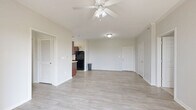 Located at 7855 Kitty Hawk Rd in Converse, TX, this single-story, 2-bedroom, 2-bathroom home offers a well-organized layout with a bright, open feel throughout. The spacious living area features light wood-look flooring and a ceiling fan with light fixture, creating a clean and airy atmosphere. It flows seamlessly toward the entry and into the hallway connecting the rest of the home.

The galley-style kitchen is outfitted with rich dark wood cabinetry, light countertops, a double sink, and black stainless appliances including a refrigerator, range, microwave, and dishwasher. A window above the counter brings in natural light.

Both bedrooms are carpeted and include ceiling fans, windows with blinds, and closet access. The generously sized primary bedroom features a walk-in closet with wire shelving extending along two walls, offering ample storage. The two bathrooms are finished with matching dark wood vanities, light countertops, and wood-look tile flooring.

Additional features include a dedicated laundry area, three closets total, and a private balcony with a wooden deck and metal railing that opens to a sweeping view of the surrounding landscape and open green space — a standout feature of this well-appointed home.