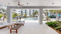 Located at 100 Boucle Jeanne Circle in Maitland, Florida, this residential community is defined by its thoughtfully designed outdoor amenity spaces and modern architectural aesthetic. The building's exterior presents a clean, contemporary facade with large dark-framed windows, private balconies with sleek metal railings, and a neutral stucco finish that complements the lush Florida surroundings.

At the heart of the community lies a generously sized resort-style pool, its clear turquoise water framed by a wide stone paver deck. Multiple private cabanas with louvered shade structures and lounge chairs line the pool's edge, offering shaded retreats surrounded by tall palm trees and tropical plantings. A covered poolside pavilion with a terra cotta roof provides additional outdoor gathering space.

Throughout the courtyard, paver walkways connect a series of distinct outdoor lounges. One features modern white modular furniture arranged on a manicured turf lawn, enclosed by lush fern beds and accented with overhead string lights. A covered seating area with a ceiling fan and natural wood-toned double doors creates a comfortable, shaded nook framed by verdant tropical foliage. Landscaping throughout is rich with palms, bamboo, banana plants, ferns, and neatly arranged shrubs, creating a layered, tropical garden atmosphere across the entire property.