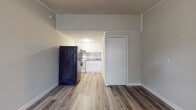 Located at 2909 Burroughs Dr in Pine Hills, FL, this single-floor unit offers a practical and well-updated layout designed for comfortable everyday living. The main living area is bright and open, featuring wood-look vinyl plank flooring in a warm gray tone that runs throughout the space. A large window with blinds allows generous natural light to fill the room, while a wall-mounted HVAC unit provides climate control. The textured ceiling adds a classic residential touch, and clean white baseboards frame the space neatly. The kitchen is efficiently designed and thoughtfully updated, showcasing white shaker-style cabinetry, granite countertops with speckled gray and white tones, a stainless steel undermount sink with a modern arc faucet, and a neutral subway tile backsplash. A white electric range and a full-size refrigerator complete the kitchen's appliance package. A closet with a paneled white door is conveniently positioned adjacent to the kitchen area. The bathroom continues the cohesive aesthetic with granite countertops on a white vanity, wood-look flooring, and clean, neutral wall finishes. The overall design palette of soft grays, whites, and natural wood tones gives the unit a clean, contemporary feel throughout.