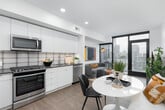 This single-floor residence showcases a thoughtfully designed contemporary interior with a cohesive, modern aesthetic throughout. The open-plan living and dining area serves as the heart of the space, centered around large floor-to-ceiling windows framed in sleek black that flood the interior with natural light and frame sweeping urban skyline views. A private balcony, accessible via a glass door, extends the living space outdoors. The living area features wood-look flooring, a comfortable seating arrangement, and curated artwork, creating an inviting yet sophisticated atmosphere.

The kitchen is efficiently designed with flat-front cabinetry in a soft grey-white finish, dark countertops, a textured tile backsplash, and a full suite of stainless steel appliances including a gas range, built-in microwave, dishwasher, and a full-size refrigerator.

The bedroom is a calm retreat highlighted by a warm terracotta accent wall, plush carpeting, and expansive windows offering additional city views. A walk-in closet provides generous storage. Exposed concrete architectural elements add an industrial character to the space.

The bathroom is cleanly finished with large-format dark floor tiles, a white vanity with dark countertop, and a framed mirror with overhead lighting.