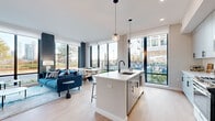 Located at 5 Port Imperial Boulevard in Weehawken, NJ, this well-appointed 2-bedroom, 2-bathroom residence offers a thoughtfully designed open-concept layout bathed in natural light. Floor-to-ceiling windows throughout create a bright, airy atmosphere while framing outdoor views of the surrounding Port Imperial waterfront community. Light hardwood flooring runs throughout the main living areas, complementing the contemporary aesthetic.

The kitchen is a standout feature, equipped with sleek light-toned cabinetry, stainless steel appliances, a large quartz-topped island with bar seating, and pendant lighting — all oriented toward the living and dining areas to facilitate an effortless flow. The living room is anchored by a bold accent wall and large windows that draw in generous daylight.

The primary bedroom is a well-proportioned retreat with expansive windows, soft blue accent walls, and ample closet space. The second bedroom offers a similarly light-filled environment. Both bathrooms are finished with modern vanities featuring wood cabinetry and white countertops; the primary bath showcases striking marble-style tile flooring, while the secondary bath includes a soaking tub. A hallway and two closets add to the functional layout of this refined urban residence.