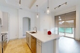 Located in Charlotte's vibrant Dilworth neighborhood, this one-bedroom, one-bathroom residence offers a thoughtfully designed single-floor layout with refined finishes throughout. The open-concept kitchen and living area serves as the heart of the home, anchored by a large central island with a white quartz countertop, undermount sink, and stainless steel appliances including a French door refrigerator, range, and built-in microwave. A classic herringbone backsplash, soft-close cabinetry, and pendant lighting above the island add elegance to the space. Warm travertine tile flows through the kitchen, transitioning to rich hardwood flooring in the living area. Floor-to-ceiling windows flood the living space with natural light and offer views of the surrounding greenery. The spacious bedroom features plush carpeting, a sliding glass door opening to an outdoor green space, a walk-in closet with built-in shelving, and direct access to the full bathroom. The bathroom impresses with travertine tile flooring, a long double vanity with a white countertop, and a fully tiled walk-in shower. A connecting hallway with an arched entry completes the clean, cohesive layout of this well-appointed Charlotte residence.