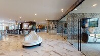 This upscale amenity space is designed with a refined, contemporary aesthetic that seamlessly blends luxury materials with functional areas. Expansive marble tile flooring with striking veining flows throughout the entire space, creating a cohesive and polished foundation. The main lounge area serves as a dramatic focal point, anchored by a sculptural tufted white sofa and adorned with richly textured, abstract-patterned wall coverings in earthy tones of charcoal and bronze. Floor-to-ceiling glass partitions separate functional zones while maintaining an open, airy feel.

A full-service bar area features dark marble countertops, pendant lighting, and barstool seating — ideal for social gatherings. Adjacent to it, a gourmet demonstration kitchen is equipped with a large stainless steel range, a suspended ventilation hood, expansive island countertops, and designer pendant lighting. The kitchen opens to a dining area furnished with a formal table and upholstered seating, bathed in natural light from large windows and glass doors leading to an outdoor terrace.

A separate lounge retreat includes a wall-mounted fireplace, curated artwork, and plush seating, while glass-enclosed private offices or meeting rooms offer a professional setting. Throughout, recessed lighting, bold artwork, and carefully curated furnishings reinforce the space's elevated, hospitality-inspired character.