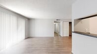 This single-floor residence presents a clean, neutral aesthetic throughout, with light gray walls, wood-style laminate flooring, and textured ceilings that carry consistently from room to room. The open living area is generously sized, benefiting from large sliding glass doors fitted with vertical blinds that invite abundant natural light and provide views of surrounding greenery. The layout flows naturally from the living space toward a dedicated dining or secondary living zone, with a pass-through kitchen visible from the main area. The kitchen is equipped with dark granite-style countertops, wood cabinetry, a full-size refrigerator, and a dishwasher, offering practical functionality. Louvered bifold closet doors are a recurring design element found in multiple rooms, providing ample storage throughout the unit. The bedrooms are well-proportioned, each featuring wood-style flooring, neutral walls, and windows that bring in natural light. One bedroom offers direct outdoor access through a sliding glass door. A dedicated bedroom includes a double bifold closet with built-in shelving and hanging rods, maximizing storage capacity. The overall ambiance is bright, clean, and versatile, providing a functional and adaptable living environment ready for personalization.
