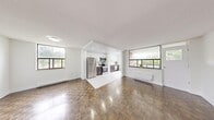 This well-designed two-bedroom, two-bathroom unit is laid out on a single floor, making efficient use of its space. The open-concept living and dining area is a standout feature, characterized by rich parquet hardwood flooring that extends throughout the unit, white walls, and a textured ceiling that adds subtle depth. Multiple large windows flood the living area with natural light and offer views of surrounding greenery, creating a bright and welcoming atmosphere. Baseboard heating units are positioned beneath the windows throughout the unit.

The kitchen is seamlessly integrated into the living space via a defined recessed area. It features modern two-tone cabinetry — white upper cabinets paired with dark lower drawers — complemented by light quartz countertops, white tile backsplash, and a full suite of stainless steel appliances including a refrigerator, electric range, and over-the-range microwave. Tile flooring distinguishes the kitchen zone from the rest of the unit.

Both bedrooms continue the parquet flooring theme and are finished with clean white walls. The primary bedroom offers a comfortable footprint, while the second bedroom features a large window with garden views. The two bathrooms are finished in white tile, with one including a soaker tub and shower combination. An in-unit laundry area completes this practical layout.