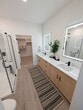 This 1,100 sq ft single-story residence at 25 Cenote Cir in St. Augustine, FL offers a well-designed 2-bedroom, 2-bathroom layout with modern finishes throughout. The open-concept kitchen and living area serves as the heart of the home, featuring light wood-toned lower cabinetry paired with crisp white upper cabinets, white quartz countertops, a tile backsplash with under-cabinet lighting, and a full suite of stainless steel appliances including a range, microwave, dishwasher, and French door refrigerator. A kitchen island provides additional prep and seating space, while pendant lighting adds a contemporary touch. Light hardwood flooring extends through the main living areas, complementing the bright, neutral color palette. Both bedrooms are carpeted and equipped with ceiling fans, offering a comfortable retreat. The 170 sq ft primary bedroom connects to a private en-suite bathroom featuring a wood-toned vanity, white quartz countertop, LED-lit mirror, and black matte fixtures. The second bathroom includes a tub-shower combination with white tile surround and matching black hardware. Two closets and a hallway complete the efficient floor plan, making this home a clean, move-in-ready space ideal for modern living.