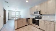 Located at 9445 FM-1464 N in Houston, TX, this thoughtfully designed one-bedroom, two-bathroom residence offers a clean, modern aesthetic across a well-utilized single floor. The open-concept kitchen and living area serves as the heart of the unit, featuring light wood-tone cabinetry, granite countertops, a tile backsplash, and a full suite of stainless steel appliances including an electric range, over-the-range microwave, and dishwasher. Wood-look luxury vinyl flooring runs throughout the main living areas, lending warmth and cohesion to the space. Natural light flows in through large windows fitted with horizontal blinds, complemented by a ceiling fan in the living area. A dedicated pantry with wire shelving provides additional storage off the kitchen. The bedroom is carpeted for comfort and includes a generous walk-in closet with built-in wire shelving, as well as a window that brings in natural light. Both bathrooms are finished with matching granite-topped vanities and the same wood-tone cabinetry found throughout the unit, maintaining a consistent design language. The primary bathroom connects directly to the bedroom, offering a convenient en-suite layout. Overall, the unit presents a cohesive, contemporary finish palette well-suited for comfortable urban living in the Houston metro area.