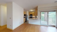 This single-floor residence is thoughtfully laid out to maximize functionality and comfort. The open-concept living area features warm hardwood-style flooring and neutral white walls, creating a bright and versatile space. Large windows and a sliding glass door flood the room with natural light while providing direct access to an outdoor deck, offering pleasant outdoor views.

The kitchen is positioned adjacent to the living area and is separated by a peninsula counter, which serves as both a workspace and casual dining surface. It is equipped with stainless steel appliances, including an electric range and refrigerator, complemented by a black over-the-range microwave. Warm-toned wooden cabinetry provides ample storage, and a double basin sink sits beneath a window. Stone-look tile flooring ties the kitchen together.

The two bedrooms are carpeted and generously proportioned, each featuring windows that bring in natural light. Closet storage is present in at least one bedroom. The unit includes two bathrooms: one features a combination tub and shower with a vanity, while the second offers a standalone shower with tile flooring. Both bathrooms maintain a clean, functional aesthetic consistent with the overall design of the space.