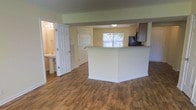 This two-story home offers a thoughtfully designed layout that balances open-concept living with functional room separation. The main level showcases warm, wood-style plank flooring that flows seamlessly throughout, lending a cohesive and inviting feel to the space.

The kitchen is anchored by a white peninsula that provides additional prep and seating space, while dark cabinetry adds a rich contrast to the light-toned walls. A chandelier-style light fixture hangs above, adding a decorative touch, and a window brings in natural light, brightening the cooking and dining area.

Adjacent to the kitchen, the open layout connects effortlessly to the surrounding living areas, creating a spacious and airy feel. The soft yellow-toned walls throughout complement the natural warmth of the flooring, contributing to an overall bright and welcoming ambiance.

A full bathroom is conveniently accessible from the main living area, complete with a pedestal sink and bright vanity lighting. Additional closet space is also available nearby, offering practical storage solutions. The combination of open sightlines, natural light, and warm finishes makes this a comfortable and well-appointed home across both floors.