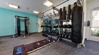 Located at 1301 Charter Colony Pkwy in Midlothian, Virginia, this single-story fitness center is designed to support a comprehensive range of workout routines. The facility is divided into distinct functional zones, each outfitted with purpose-specific equipment and finishes.

The main workout area features patterned carpet flooring and is anchored by a vibrant teal accent wall that gives the space an energetic character. Flush-panel ceiling lights provide consistent, bright illumination throughout. Along one wall, a fully stocked rack displays an extensive collection of kettlebells, medicine balls, and free weights, complemented by a mounted heavy punching bag for combat-style training. A functional trainer cable machine occupies the central area, while large mirrors along one wall expand the sense of space and allow users to monitor form.

The cardio section lines the perimeter with multiple Matrix treadmills, an upright cycle, and a stair climber, with windows allowing natural light to filter in. A wall-mounted television keeps users engaged during longer sessions.

A separate spin studio features light vinyl flooring, clean white walls, and large windows offering natural views. Several stationary cycling bikes and a set of stability balls are housed here, along with double doors providing convenient storage access. Together, these spaces form a cohesive, well-appointed fitness facility.