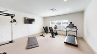 Located at 100 Marcus Byers Dr in Huntsville, Alabama, this dedicated exercise room offers a clean and functional space designed to support a variety of fitness routines. The room is finished with neutral-toned carpeting and bright white walls, creating a clean, open atmosphere that encourages activity. Recessed lighting throughout the ceiling, complemented by a centrally mounted HVAC unit, ensures a comfortable environment year-round. A large window along one wall allows natural light to filter in, offering outdoor views that help energize workouts. The space is outfitted with an array of fitness equipment, including a treadmill, stationary bike, a multi-function cable and strength training machine, a dumbbell rack, and a flat exercise mat for stretching or floor exercises. A wall-mounted flat-screen television provides entertainment or instructional content during workouts. A stainless steel waste receptacle adds a polished, functional detail to the room. The layout is thoughtfully arranged to maximize usable floor space while keeping equipment accessible and organized. A refrigerator positioned near the entry provides convenient access to refreshments. This self-contained fitness facility delivers a comprehensive workout experience in a compact, well-maintained setting.