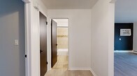 This single-floor, one-bedroom, one-bathroom unit at 265 Lowrey Pl in Newington, CT offers a well-organized layout that maximizes its compact footprint. Light wood-tone laminate flooring runs consistently throughout the space, creating a cohesive and clean aesthetic.

The combined kitchen and living area forms the heart of the unit. The kitchen features white shaker-style cabinetry with black hardware, granite-look countertops, a double sink, and white appliances including a gas range and refrigerator. A sliding glass door connects the kitchen/living area to an outdoor deck, allowing natural light to fill the space and providing convenient outdoor access.

The living area is accented by a bold dark feature wall, contrasting with the otherwise neutral white walls and creating a modern focal point. A wall-mounted air conditioning unit and baseboard heating serve the space.

The spacious primary bedroom includes a large double-door closet and cool-toned gray walls, continuing the light flooring. Dark interior doors provide a consistent design contrast throughout the unit.

A hallway connects the bedroom to the full bathroom, which features beige floor and wall tiles, a tiled tub-shower combination with a decorative mosaic accent band, a wood-toned vanity with a white basin, black fixtures, and a framed mirror.