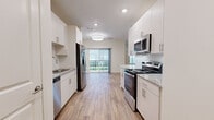 Located at 131 Great Circle Rd in Nashville, TN, this thoughtfully designed single-floor unit offers a modern, open-concept layout making efficient use of its compact footprint. The kitchen is a standout feature, showcasing white shaker-style cabinetry extending to the ceiling, granite countertops, a peninsula with bar seating illuminated by pendant lighting, and a full suite of stainless steel appliances including a range, microwave, dishwasher, and refrigerator. Light wood-tone luxury vinyl plank flooring runs throughout, creating a cohesive and contemporary aesthetic. Recessed lighting and a central flush-mount fixture keep the space bright and well-lit. A sliding glass door at the end of the main living area opens to a private balcony, allowing natural light to flood the interior and providing outdoor views. The bathroom continues the unit's refined finishes with a granite-topped vanity, white cabinetry, and a large mirror. A dedicated closet space includes built-in shelving and houses an in-unit top-load washer, adding everyday convenience. Clean white walls and consistent flooring throughout lend the space a fresh, move-in-ready quality well-suited to urban living in Nashville.