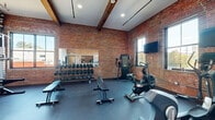 Located at 433–435 Harris Ave in Providence, Rhode Island, this fitness center combines industrial character with modern workout functionality. The space is defined by its striking exposed red brick walls and original wood beam ceilings, lending an authentic warehouse aesthetic that reflects the building's architectural heritage. Rubber flooring throughout provides a durable, safety-conscious surface suited for a variety of training activities.

The facility is divided into distinct workout zones. The cardio area is equipped with treadmills, elliptical machines, and air bikes, all positioned beneath wall-mounted flat-screen televisions and alongside multiple windows that allow natural light to fill the space and provide views of the surrounding Providence streetscape. A dedicated strength training zone features a comprehensive dumbbell and kettlebell rack system, adjustable benches, and a multi-function cable and weight machine, with large wall mirrors installed to assist with form and expand the sense of space.

A separate functional training area includes open floor space, wall-mounted exercise mats, a medicine ball rack, and a power rack with weight plates. A wall-mounted HVAC unit ensures climate control year-round. The overall ambiance is energetic yet refined, blending the raw industrial character of the building's original architecture with a fully outfitted, contemporary fitness environment.
